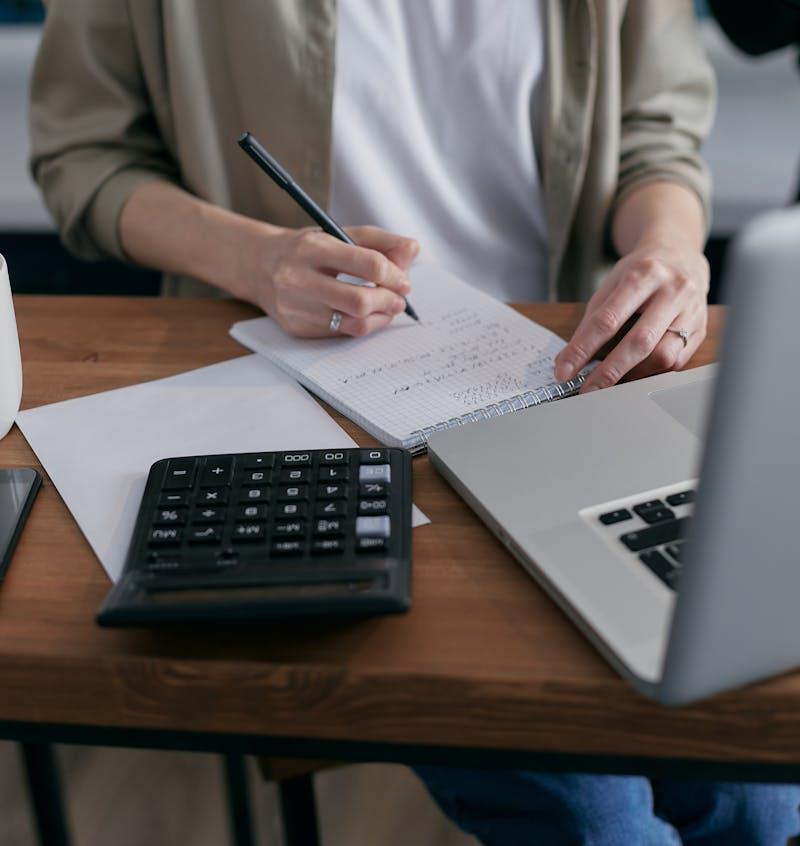 Mujer calculando en libreta con portátil